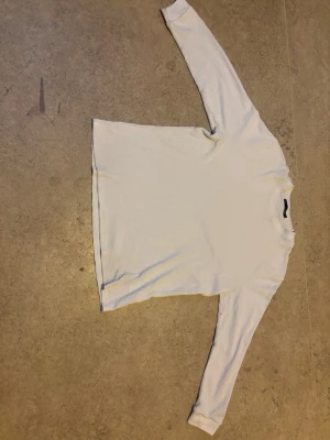 Vit långärmad tröja  - En basic vit långärmad tröja i ribbad bomull med rund halsringning. Perfekt att styla lager på lager eller bära som den är. Enkel och stilren design som passar till det mesta.