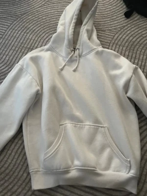 Vit hoodie från BikBok med huva - Klassisk vit hoodie från BikBok i storlek XS. Hoodien har en stor huva med dragsko, magficka och ribbade muddar vid ärmslut och nederkant. Tillverkad i mjukt och skönt material, perfekt för en avslappnad stil.
