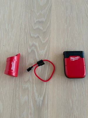 Milwaukee powerbank med USB-kabel - Röd och svart powerbank från Milwaukee med tillhörande USB-kabel och batteriadapter som funkar med värmekläder från Milwaukee  Kompakt design i plast, perfekt för att ladda dina enheter på språng. Snygg och tålig med tydlig logga på både powerbank och adapter.