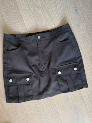 Svart kjol med fickor - Snygg svart kjol i cargo modell med stora fickor framtill och dekorativa knappar.