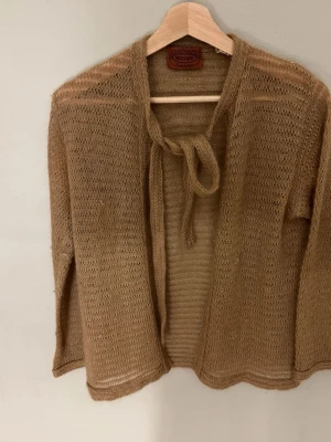 Missoni Beige meshig kofta med knytband - Säljer en beige, tunn och meshig kofta från Missoni. Koftan har långa ärmar och ett snyggt knytband framtill. Materialet är lätt och luftigt, perfekt för lager på lager. Enkel att styla till olika outfits. Missfärgning under armhålorna. 0771