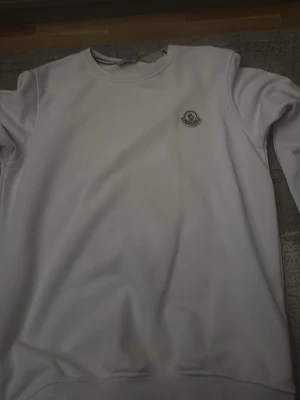 Vit sweatshirt från Moncler - Snygg vit sweatshirt från Moncler med rund halsringning och diskret Moncler-logga på bröstet. Tröjan har en klassisk passform och är tillverkad i mjukt material som känns skönt mot huden. Perfekt för en clean och stilren look.