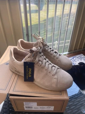 Beige sneakers från Polo Ralph Lauren - Stilrena beige sneakers i mocka från Polo Ralph Lauren. Skorna har klassisk låg profil, matchande beige snörning och diskret logga på sidan. Perfekta för dig som gillar en clean och enkel look med premiumkänsla. Dom är använda 2 gånger men bortsett från det helt nya storlek 44 men passar bäst till 45 kvitto finns