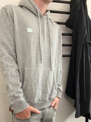 Ljusgrå hoodie från les deux - Säljer en stilren ljusgrå hoodie med huva och dragsnören. Hoodien har en klassisk känguruficka framtill och ribbade muddar vid ärmslut och nederkant. Liten patch med diskret logga på bröstet. Perfekt för en chill och avslappnad look.