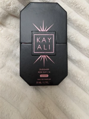 Kayali Oudgasm Rose Oud Intense 50ml - Kayali Oudgasm Rose Oud Intense är en lyxig parfym i en svart, åttakantig flaska med gulddetaljer och rosa text. Doften är en eau de parfum och flaskan rymmer 50 ml. Förpackningen matchar flaskan med samma eleganta design.