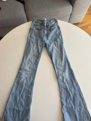 Ljusblå bootcut jeans med hög midja - Säljer ett par ljusblå jeans med bootcut-modell och hög midja. Klassisk femficksdesign och dragkedja med knapp. Jeansen har en avslappnad passform och är tillverkade i denim med lätt stretch för extra komfort.
