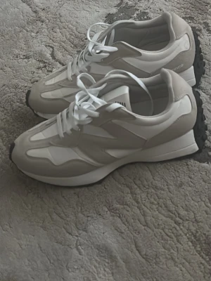 Beige och vita sneakers med chunky sula - Snygga sneakers i beige och vitt med en chunky sula och vita skosnören. Ovandelen är i en mix av mocka och textil, med en tydlig sicksack-design på sidan. Yttersulan är svart och ger bra grepp. Perfekta för en trendig och avslappnad stil.