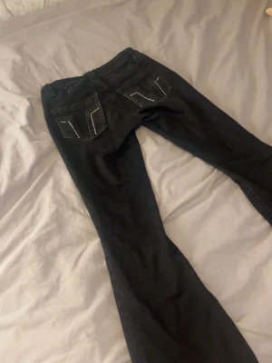 Svarta jeans med nitar på bakfickor - Säljer ett par svarta jeans med raka ben och snygga detaljer i form av silverfärgade nitar på bakfickorna. Jeansen har klassisk femficksdesign och bälteshällor. Perfekta för dig som vill ha en cool och stilren look.