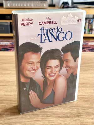 Three to Tango – VHS – ny och inplastad - Säljer Three to Tango (1999) på VHS med Matthew Perry och Neve Campbell.  Filmen är fortfarande inplastad och oöppnad, vilket gör detta till ett extra fint exemplar för samlaren eller för dig som gillar filmer och fysisk media från 90-talet. 📼  Plasten har rester från en äldre prisetikett på framsidan – se bild.  Skick: Ny / oöppnad / inplastad Format: VHS  Skickas väl emballerad.