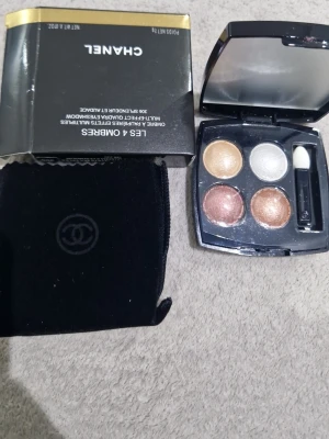 Chanel Les 4 Ombres ögonskuggspalett - Snygg ögonskuggspalett från Chanel med fyra skimrande nyanser: guld, silver, koppar och brons. Kommer i en elegant svart dosa med spegel och applikator. Perfekt för att skapa olika ögonlooks. Originalförpackning och sammetsfodral medföljer.