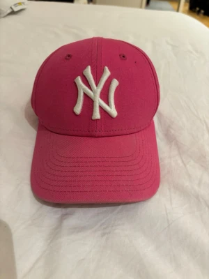 Rosa New York Yankees keps - Säljer en snygg rosa keps från New Era med New York Yankees-logga broderad i vitt framtill. Klassisk böjd skärm och justerbar rem bak. Tillverkad i bomullstyg och perfekt för dig som vill sticka ut med en färgglad accessoar.