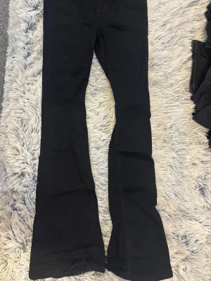 Svarta snake flare jeans från 157 - Säljer ett par svarta flare jeans från 157 i modellen Snake Flare. Jeansen har hög midja, utsvängda ben och klassisk femficksdesign. Perfekta för dig som gillar en retroinspirerad look med mycket attityd.