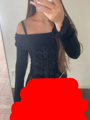 Svart offshoulder topp i sammet - Snygg svart offshoulder topp i mjuk sammet med långa ärmar. Toppen har en figurnära passform och en unik struktur i tyget som ger en cool look. Perfekt att styla med både jeans och kjol.