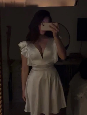 Vit klänning med volang - Säljer nu min fina studentklänning. Endast använd på studenten. Köpt från Zalando, men säljs ej mer. Vit kortklänning i satin med omlottdesign och volangdetaljer vid axlarna. Dragkedja i ryggen. Klänningen har djup v-ringning och markerad midja. Skriv privat vid fler bilder/ frågor!