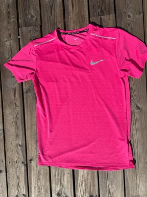 Rosa Nike löpartröja herr - Snygg rosa löpartröja från Nike med reflekterande detaljer på axlarna och logga på bröstet. Tillverkad i ett lätt och snabbtorkande funktionsmaterial som passar perfekt för träning och löpning.
