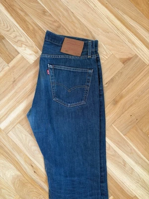 Levi's 501 jeans  - Klassiska blå jeans från Levi's med rak passform och femficksdesign. Jeansen har en mörkblå tvätt, tydliga sömmar och den ikoniska röda Levi's-lappen på bakfickan. Tillverkade i slitstarkt denimtyg, perfekta för en avslappnad stil.