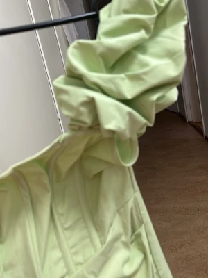 Ljusgrön axelbandslös klänning - Trendig ljusgrön klänning med axelbandslös design och voluminös detalj upptill. Klänningen har en figurnära passform och är sydd i ett slätt tyg som ger en modern look. Perfekt för dig som vill sticka ut med en unik och stilren outfit.