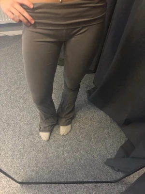 Grå yogapants - Säljer ett par grå yogapants från Nelly i storlek XS. De har utsvängda ben och bred linning i midjan för en snygg och bekväm passform. Materialet är stretchigt och mjukt, perfekt för en trendig och avslappnad look.