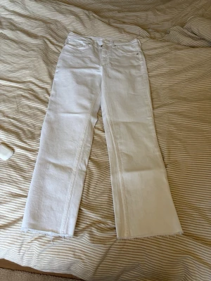 Vita raka jeans med rå kant , kortare ben modell. - Säljer ett par vita jeans med rak passform och råa, fransiga benslut. Jeansen har klassisk femficksdesign och stängs med knapp och dragkedja. Perfekta för dig som vill ha en clean och stilren look med en liten edge.
