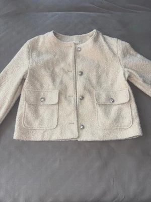 Höst jacka Zara bouclé - Säljer denna jättefina Zara-jacka som aldrig är använd och är i nyskick. Den är perfekt för hösten, eftersom den är varm och skön samtidigt som den känns väldigt stilren.  Det jag gillar mest med den är de vackra smyckesknapparna och de fina detaljerna, som gör att jackan ser mycket mer exklusiv ut. Den passar lika bra till jeans och sneakers som till en klänning eller finare outfit.  Storlek: M Färg: Offwhite/kräm Skick: Aldrig använd (nyskick)🤍