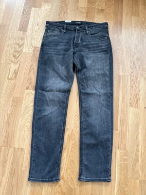 Mörkgrå raka jeans - Snygga mörkgrå jeans med rak passform och klassisk femficksdesign. Jeansen har subtila slitningar och är tillverkade i ett mjukt denimtyg som ger en avslappnad look. Perfekta för dig som gillar en stilren och enkel vibe.