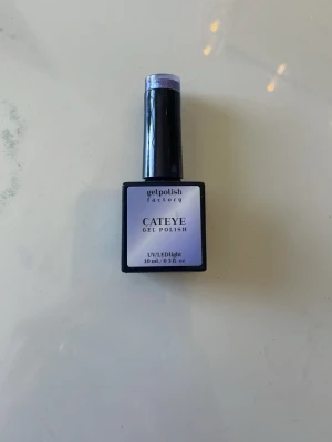 Lila Cat Eye gelnagellack - Snyggt lila Cat Eye gelnagellack som ger en skimrande och magnetisk effekt på naglarna. Kommer i en fyrkantig flaska med svart lock och innehåller 10 ml. Perfekt för dig som vill ha en unik och glittrig look på naglarna. Den är använd men typ hälften kvar.