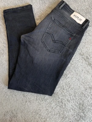 Mörkgrå Replay jeans herr - Snygga mörkgrå jeans från Replay med klassisk femficksmodell och diskreta slitningar. Jeansen har raka ben och en stilren bakficka med broderad detalj. Perfekta för en avslappnad men trendig look.