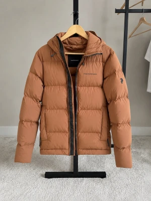 Peak Performance Rivel Down Jacket (Herr) - Säljer en riktigt varm och rejäl dunjacka från Peak Performance (modell Rivel / G77962) i färgen sierra sand.   Jackan är perfekt för kalla vinterdagar och håller både vind och lättare regn/snö ute tack vare sitt vind- och vattenavvisande yttertyg. Jackan användes en gång bara och säljs då storleken inte passar längre.