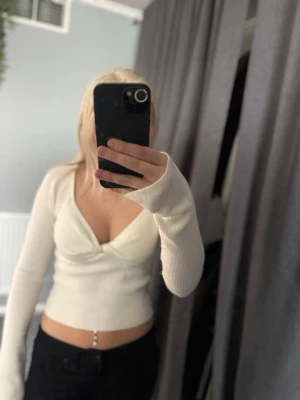 Vit ribbad croppad topp från NA-KD - Säljer en vit ribbad croppad topp från NA-KD i storlek XS. Toppen har lång ärm, v-ringning och twistad detalj framtill. Perfekt för dig som gillar en enkel men snygg stil. Materialet är mjukt och stretchigt.