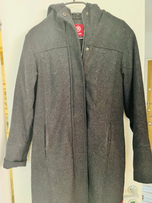 Vintage Mörkgrå kappa med huva från Redlabel - Snygg mörkgrå kappa från Redlabel i storlek XS. Kappan har huva, dragkedja framtill och två diskreta fickor. Materialet är tjockt och quiltat på insidan för extra värme. Perfekt för kyliga dagar och stilren look.