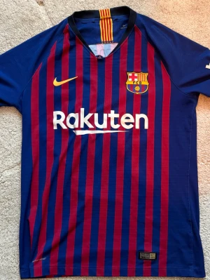 Barcelona matchtröja Coutinho #14 - Säljer en officiell FC Barcelona matchtröja från Nike med vertikala blå och vinröda ränder. Tröjan har tryck med Coutinho och nummer 14 på ryggen, samt klubbmärke och sponsorloggor på bröstet. Tillverkad i lätt och ventilerande material, perfekt för fotbollsträning.