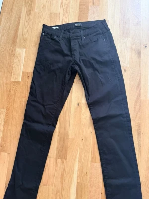 Svarta slim fit jeans - Säljer ett par svarta slim fit jeans med klassisk femficksdesign och raka ben. Jeansen har en enkel look utan slitningar eller dekorationer, perfekta för en clean och stilren outfit. Materialet känns mjukt och stretchigt för extra komfort.