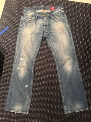 Jack & Jones vintage denimjeans - Säljer ett par ljusblå jeans med slitningar och distressed detaljer på både fram- och baksida. Jeansen har raka ben, klassiska fem fickor och synliga sömmar. Perfekta för en avslappnad och trendig look.