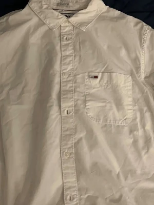 Vit skjorta från Tommy Jeans - Klassisk vit skjorta från Tommy Jeans med bröstficka och liten logga. Skjortan har knappar framtill, krage och en clean look som passar till många stilar. Regular fit och tillverkad i bomull för en skön känsla. Nypris runt 1 lappen