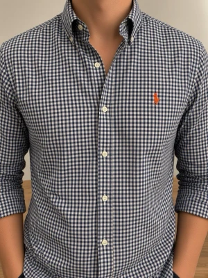Rutig skjorta från Polo Ralph Lauren (Slim Fit) - Säljer en klassisk långärmad skjorta från Ralph Lauren i blåvitt rutigt mönster. Skjortan har knappar framtill, button-down krage och den ikoniska broderade loggan i orange på bröstet. Perfekt till jeans eller chinos för en clean look. Storlek M. Snabb Leverans!