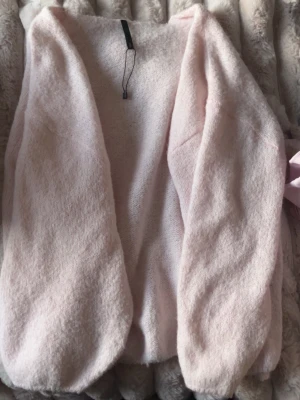 Ljusrosa kofta - Mysig ljusrosa kofta med öppen front och lång ärm. Koftan är fluffig och har en avslappnad passform, perfekt att slänga på sig när det är lite kyligt. Materialet känns mjukt och skönt mot huden.