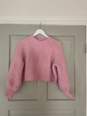 Rosa stickad tröja från ZARA - Söt rosa stickad tröja från ZARA med croppad passform och ballongärmar. Tröjan har rund halsringning och är gjord i ett mjukt, ribbstickat material som känns både trendigt och bekvämt. Perfekt för dig som vill ha en mysig men ändå stylish look.