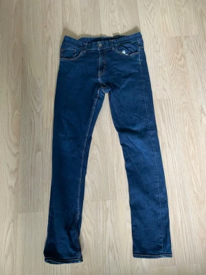 Mörkblå raka jeans - Säljer ett par mörkblå jeans med rak passform och klassiska fem fickor. Jeansen har kontrastsömmar och är tillverkade i ett mjukt denimtyg. Perfekta för en avslappnad och stilren look.