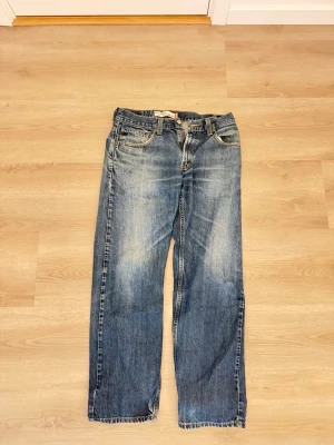 Levi's 559 blå jeans W32 L32 - Klassiska blå jeans från Levi's modell 559 med raka ben och fem fickor. Jeansen har en snygg tvättad look med slitningar och är tillverkade i slitstark denim. Perfekta för en avslappnad och trendig stil.