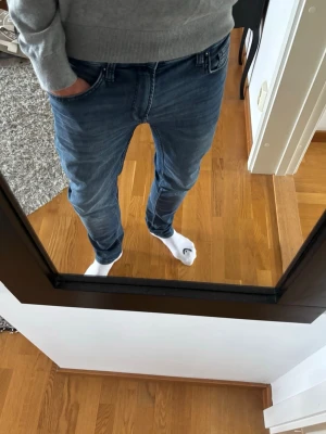 Blå slim fit jeans herr - Snygga blå slim fit jeans med klassisk femficksdesign och normalhög midja. Jeansen har en lätt tvättad look och smal passform som sitter tajt över benen. Perfekta för en avslappnad och trendig stil.