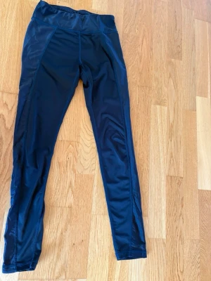 Svarta sportiga leggings - Snygga svarta leggings med hög midja och smal passform. Tillverkade i ett stretchigt och glansigt material som passar perfekt till träning eller chill. Sömmar längs benen ger en sportig look och de sitter skönt på kroppen. Nästan aldrig använda 