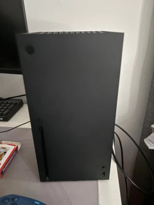 Xbox Series X spelkonsol svart - Säljer en Xbox Series X spelkonsol i mattsvart färg med stilren, rektangulär design och ventiler på ovansidan med grön accent. Perfekt för gaming med kraftfull prestanda och stöd för 4K-upplösning. Passar dig som vill ha den senaste tekniken i snyggt format. Två kontroller ingår i priset 