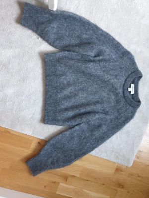 & Other stories Grå fluffig stickad tröja - Mysig grå stickad tröja i Mohair med rund hals och långa ärmar. Tröjan har en fluffig och mjuk struktur, perfekt för kyliga dagar. Enkel och stilren design som passar till det mesta. Ribbstickade muddar vid ärmslut och nederkant.