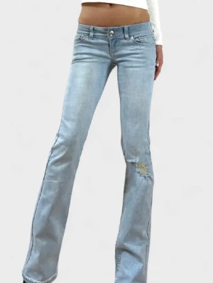 Ljusblå bootcut jeans med slitning - Säljer ett par ljusblå bootcut jeans med super låg midja och slitning på ena låret. Jeansen har klassiska fem fickor, dragkedja och knapp framtill samt snygga sömdetaljer bak. Perfekta för en avslappnad och trendig look. Köpta men har aldrig kommit till användning 