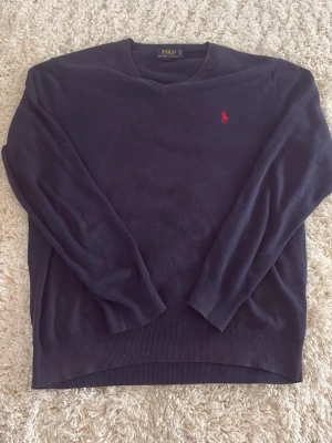Mörkblå stickad tröja från Polo Ralph Lauren - Mörkblå stickad tröja från Polo Ralph Lauren med klassisk röd broderad logga på bröstet. Tröjan har rund halsringning, långa ärmar och ribbade muddar vid ärmslut och nederkant. Perfekt för en stilren och avslappnad look. Kom dm för frågor🙏❤️