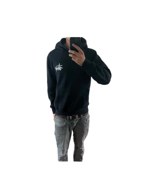 Svart Stüssy hoodie med logga - Svart hoodie från Stüssy i storlek S men passar också M. Den har en vit logga på bröstet och stor grafisk logga på ryggen. Klassisk passform med huva och ribbade muddar. Perfekt för dig som gillar streetwear och vill ha en stilren men ändå statement look. Modellen i bilden är 180cm och väger 69kg, och bär vanligtvis storlek M. Fraktas snabbt📦 Skriv vid funderingar
