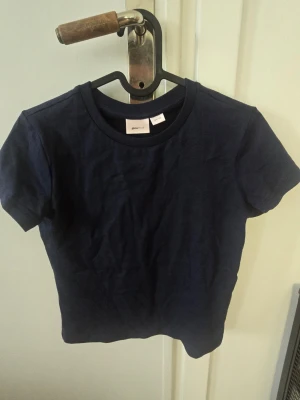 Mörkblå t-shirt från Gina Tricot - En enkel och stilren mörkblå t-shirt från Gina Tricot. T-shirten har rund halsringning och korta ärmar. Tillverkad i mjukt bomullsmaterial som känns skönt mot huden. Perfekt basplagg att matcha med olika outfits. Använd en gång.