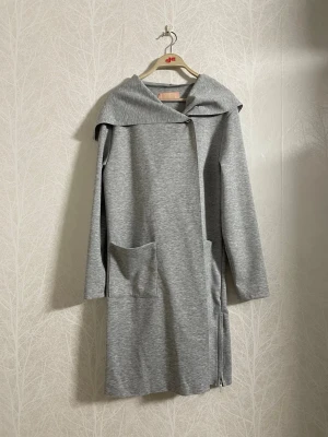Grå Amisu hoodie/cardigan - Säljer en lång, gråmelerad hoodie/cardigan i mjukt material med stora fickor och dragkedjor vid ärmslut och sidor. Köpt från New Yorker. Perfekt för en chill och avslappnad look!