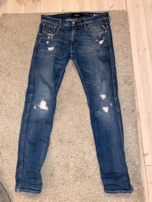 Blå slitna jeans från Replay - Säljer ett par replay Anbass med slitningar storlek 32, skick 7/10