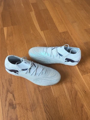 Puma Future 9 Ultimate Dreamrush - Säljer ett par ljusblå fotbollsskor från Puma med klassisk snörning och låg profil. Skorna har svartblå Puma-loggor på sidorna och är tillverkade i ett syntetmaterial som ger bra grepp på planen. Perfekta för dig som vill ha stilrena och funktionella skor till matchen. Använda en gång. Storlek 40 1/2. Nypris 2800. Påse förekommer